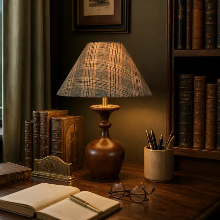 Vintage wooden table lamp with plaid shade illuminating a study desk with antique books and glasses