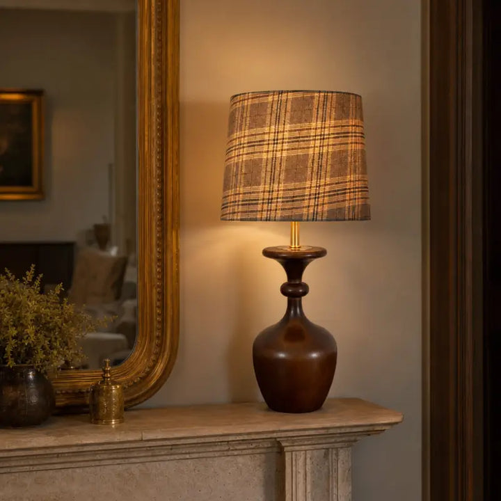 Mid century modern wood table lamp with plaid fabric shade placed on an elegant classic fireplace mantel