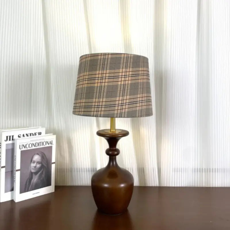 Turned wood accent lamp with grey plaid fabric drum shade standing on a dark brown wooden tabletop