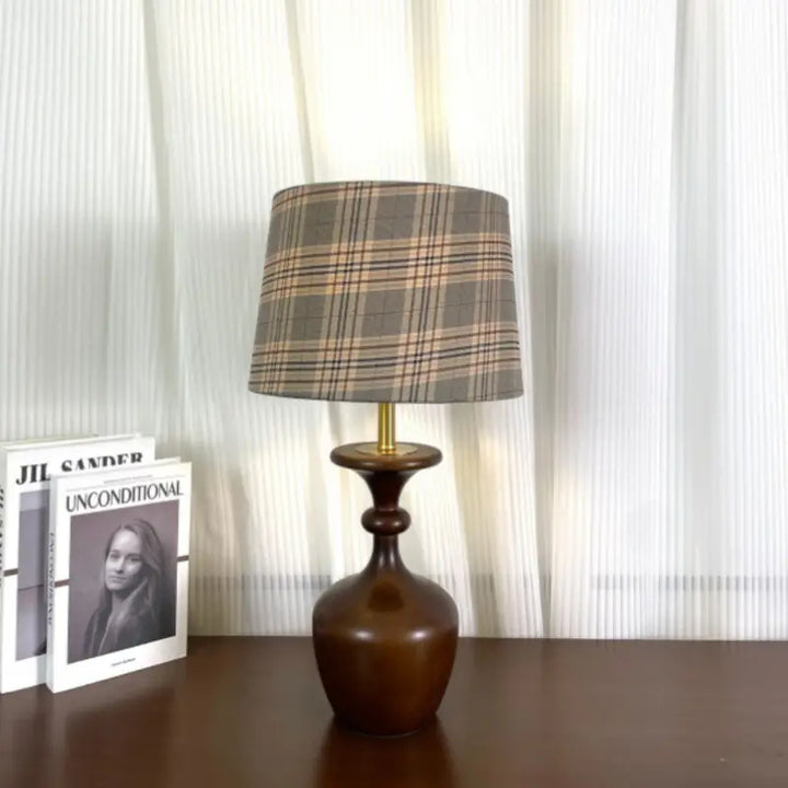 Turned wood accent lamp with grey plaid fabric drum shade standing on a dark brown wooden tabletop
