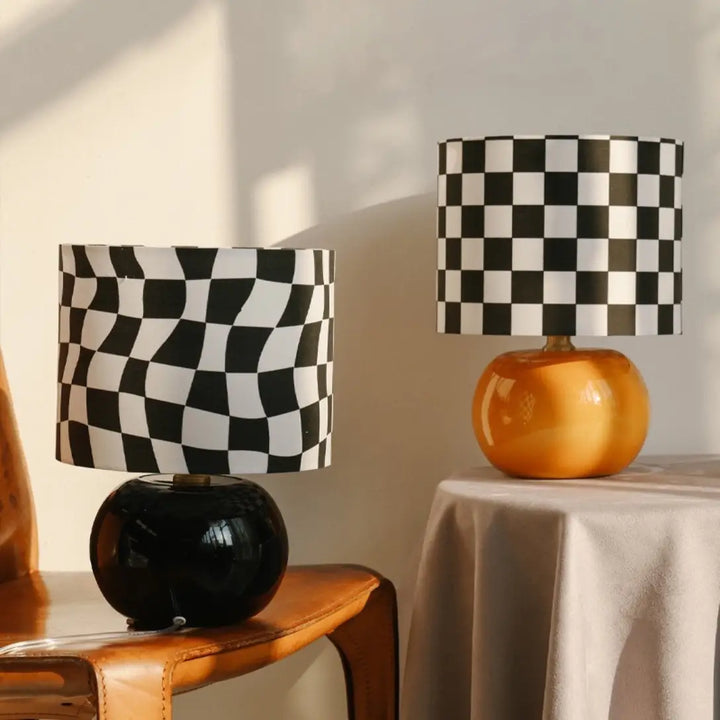 Pair of retro checkerboard glass table lamps in glossy black and orange round bases with regular and wavy checkered fabric drum shades in sunlit living room