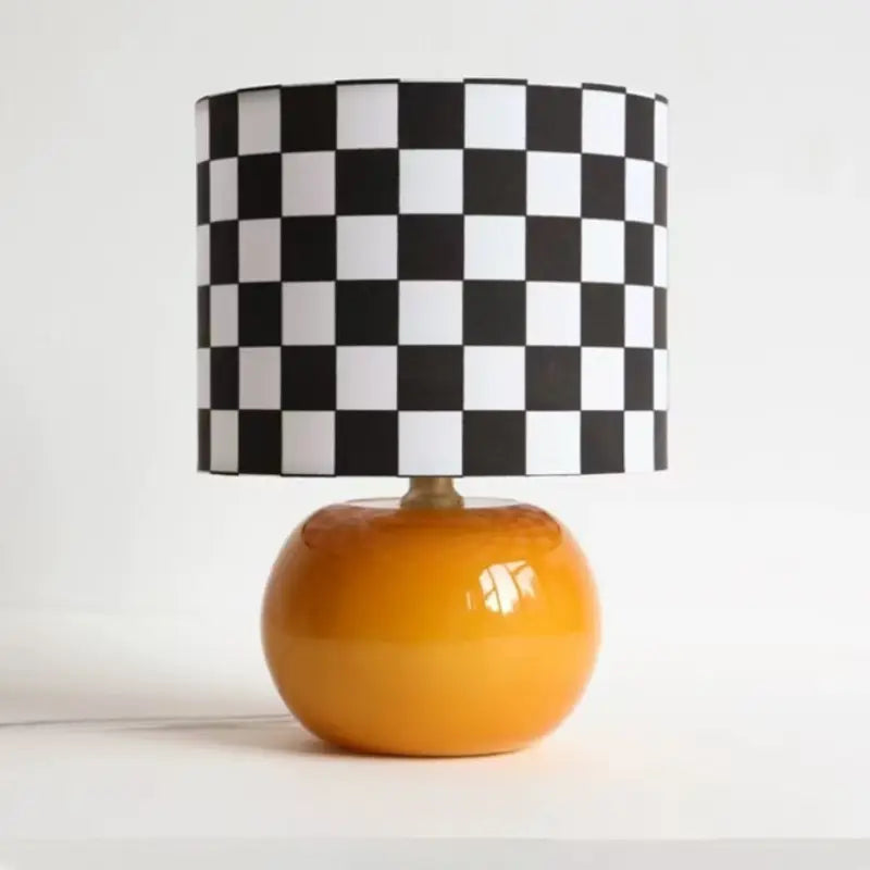 Checkerboard table lamp with glossy orange round orb glass base and black and white square grid drum lampshade isolated on white background