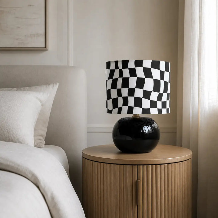 Contemporary black wavy checkerboard bedside lamp on fluted oak nightstand with neutral linen bed decor and soft ambient window light