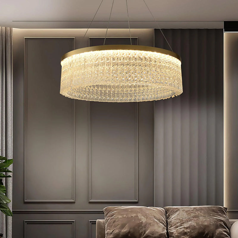 Elegant crystal chandelier with layered glass elements above a sofa in a modern living room with paneled walls and warm lighting