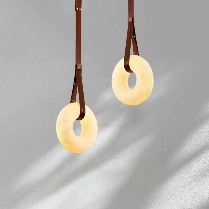 Dual Leather Strap Alabaster Donut Pendant Lights staggered hanging on grey interior wall