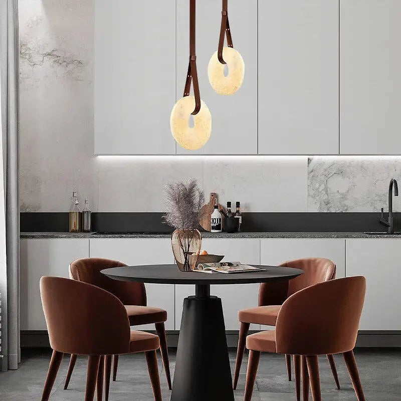 Paired Leather Strap Alabaster Donut Pendant Lights above round kitchen island dining table
