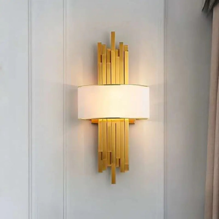 Art Deco gold stacked bar wall sconce with white fabric lampshade mounted on white wainscot panel for elegant residential interior decor