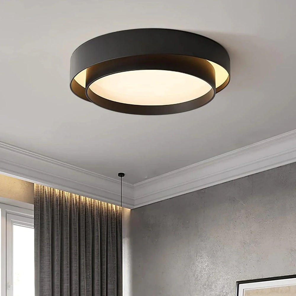 Black circular ceiling light with layered ring design mounted on a white ceiling in a living room with curtains and wall decor