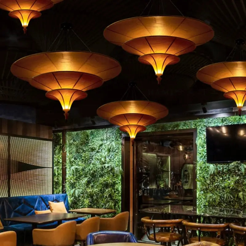Multiple Thai umbrella‑shaped pendant lamps providing ambient lighting for restaurant dining area with green plant wall decor