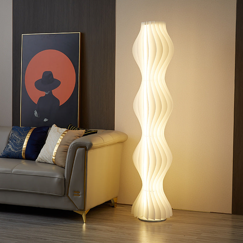 Vapor Floor Lamp with sculptural wavy design casting warm ambient light beside sofa in modern living room with wall art