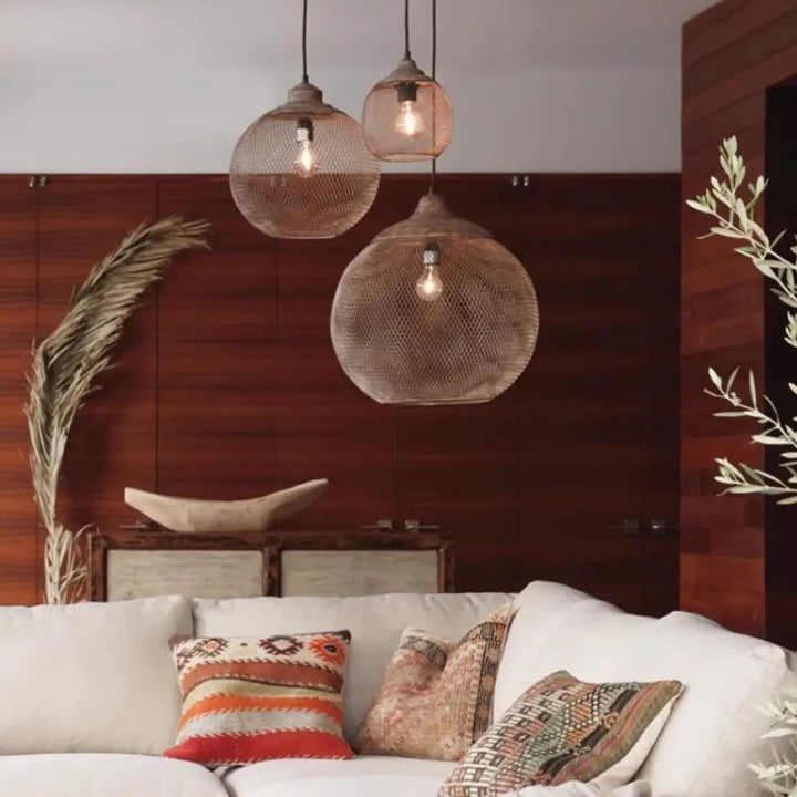 Cluster of three wire mesh sphere pendant lamps glowing above a cozy living room sofa