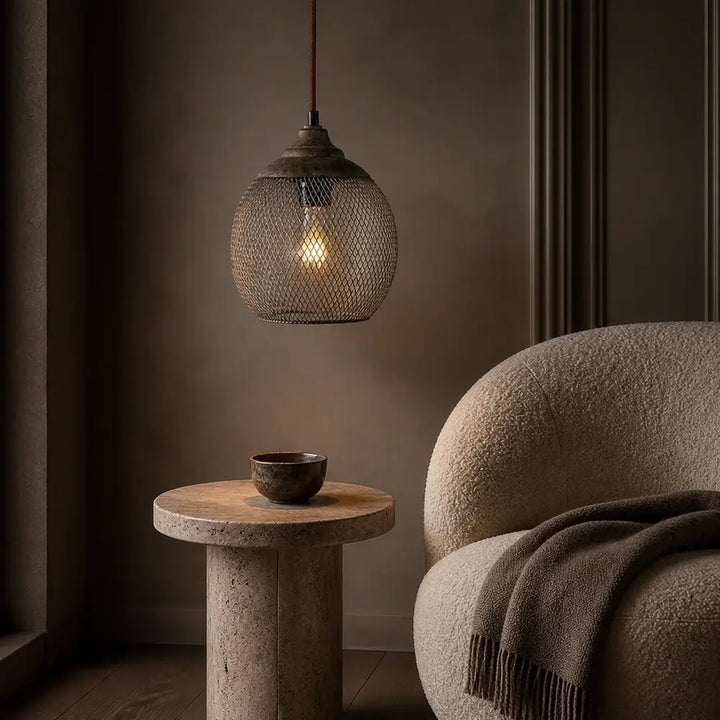Rustic mesh sphere pendant lamp hanging above round travertine table in cozy armchair corner