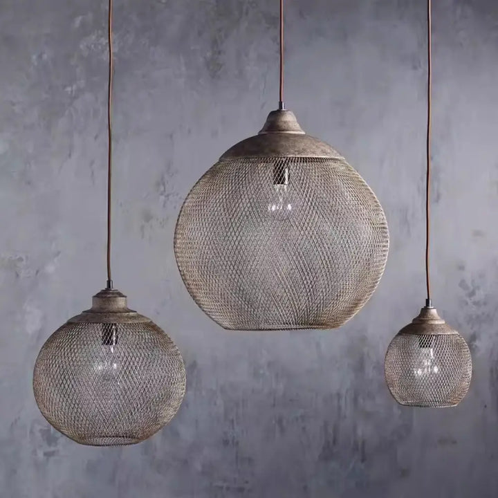 Trio of different sized wire mesh pendant lights hanging in a cluster against concrete wall