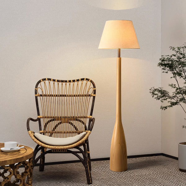 Minimalist wooden floor lamp with a beige fabric shade, placed beside a rattan chair in a cozy and natural-style living space