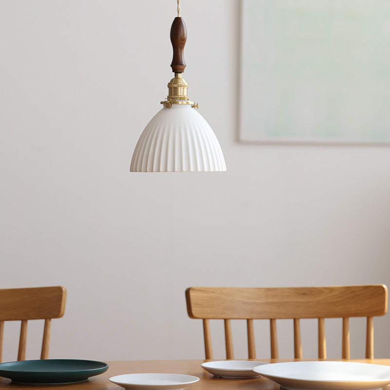 White Ceramic Pendant Light with ribbed shade, brass hardware and wooden detail, hanging above a dining table with wooden chairs in a minimalist interior.