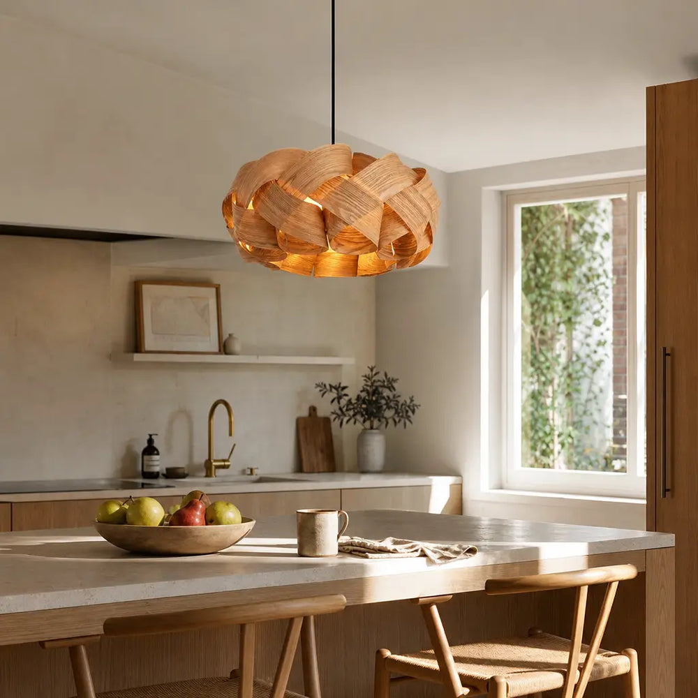Woven wood veneer chandelier hanging above kitchen island with fruit bowl and stools