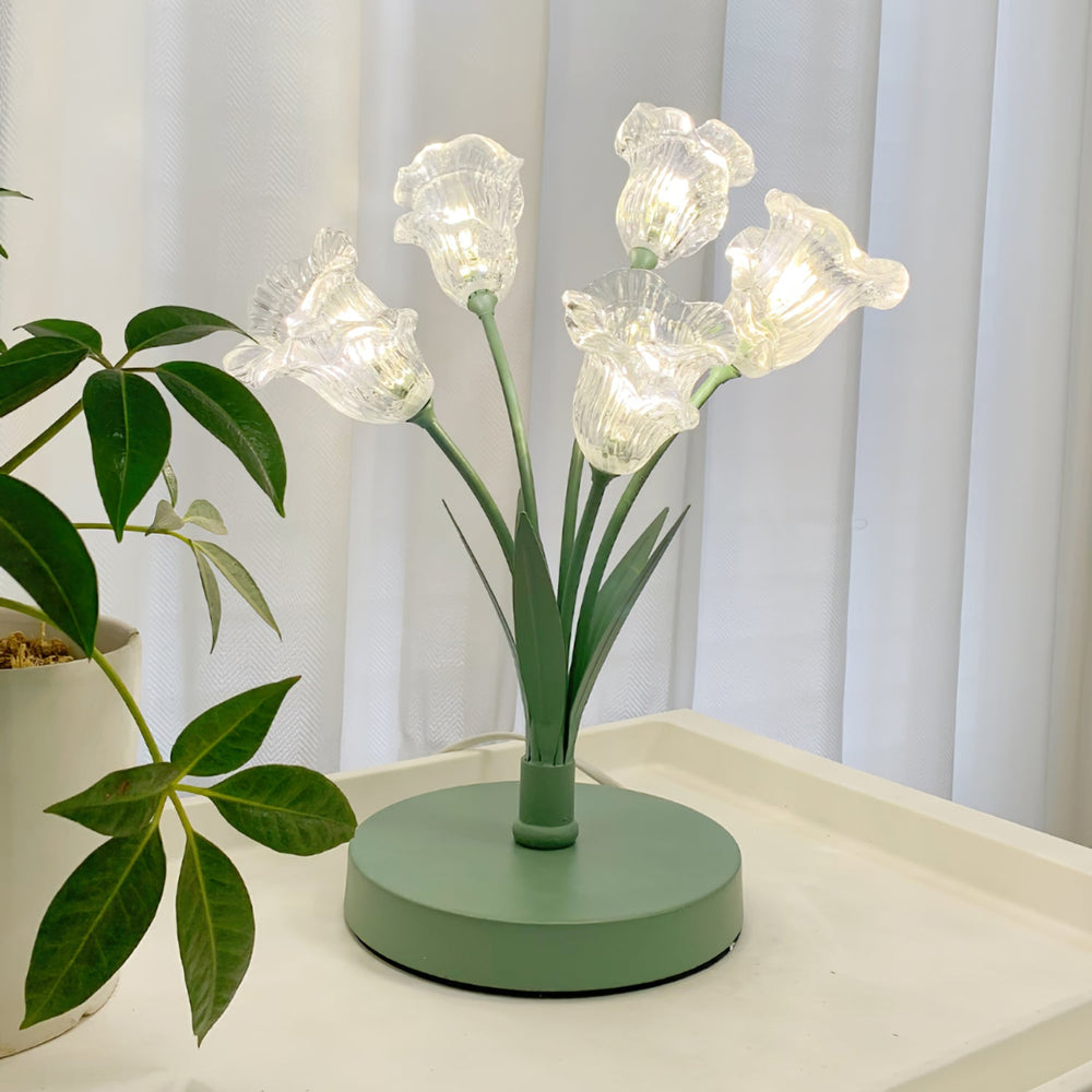 Tulip bouquet table lamp with glowing glass flowers and green base on a bedside tray next to a plant